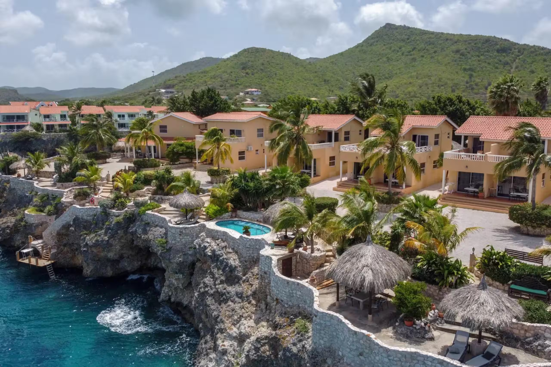 Aerial view of the resort on the cliff above the sea with thatched palapas, stone terraces and a small plunge pool