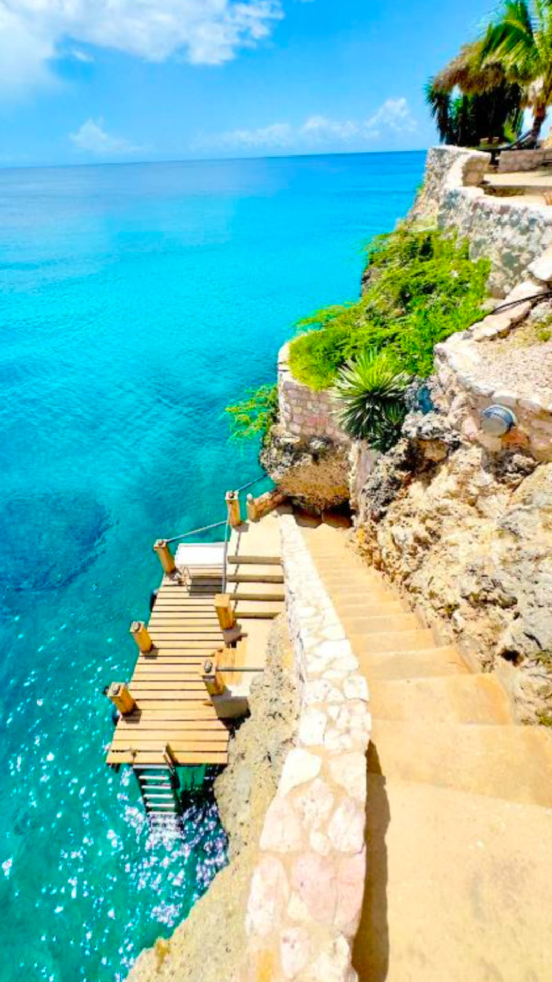 Wooden swim deck with a swim ladder and stone steps leading down the cliff into turquoise water