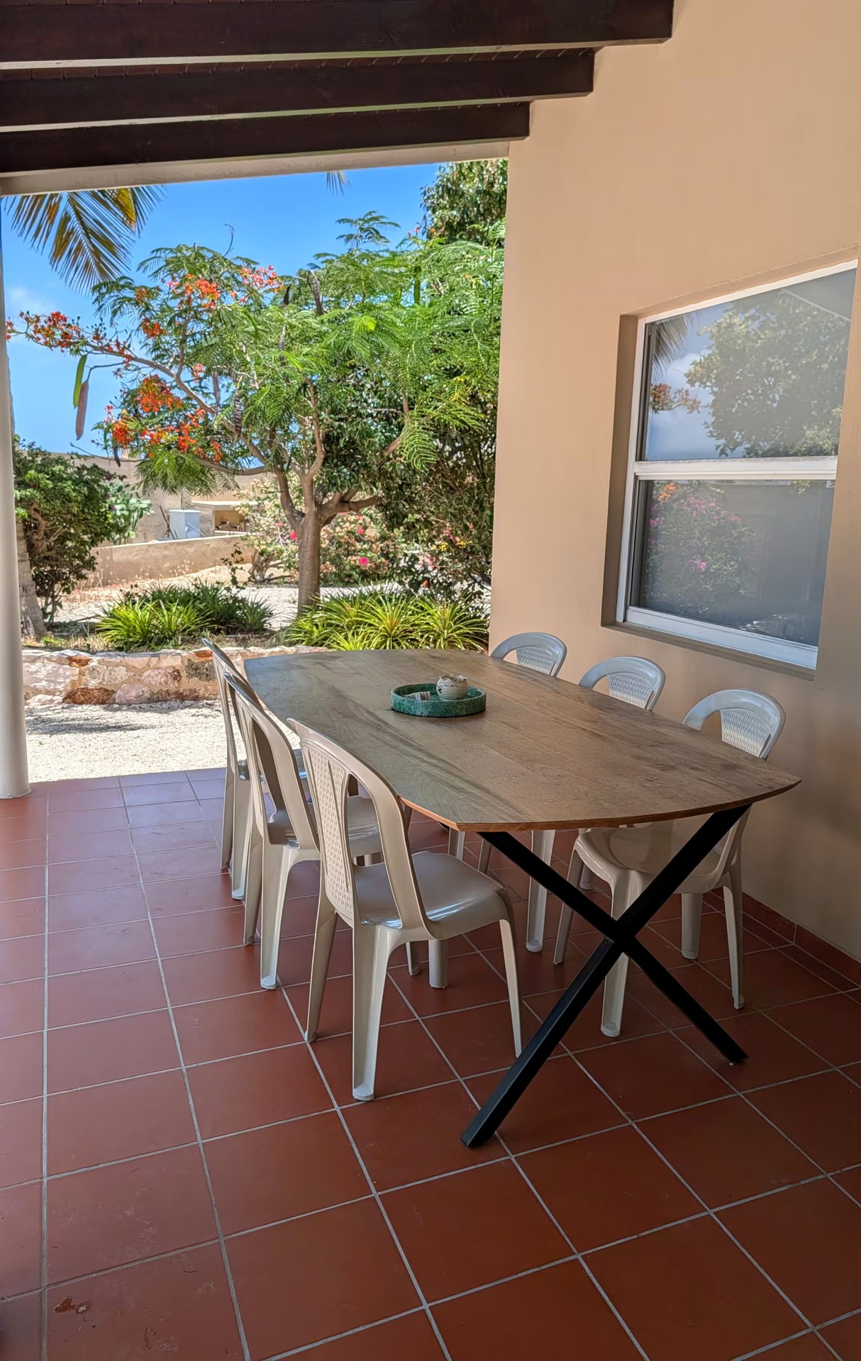 The shaded covered terrace of Huisje 21 with outdoor dining table and tropical garden