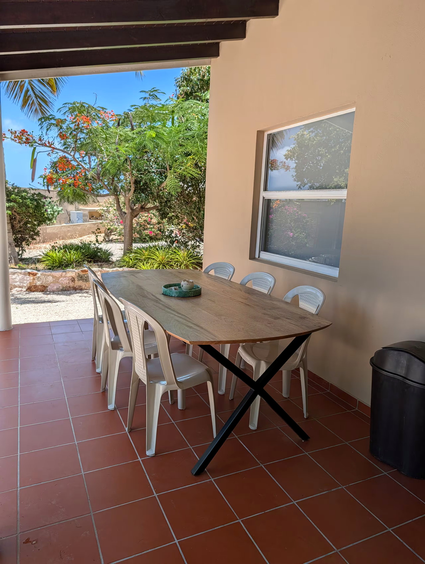 The shaded covered terrace of Huisje 21 with outdoor dining table and tropical garden