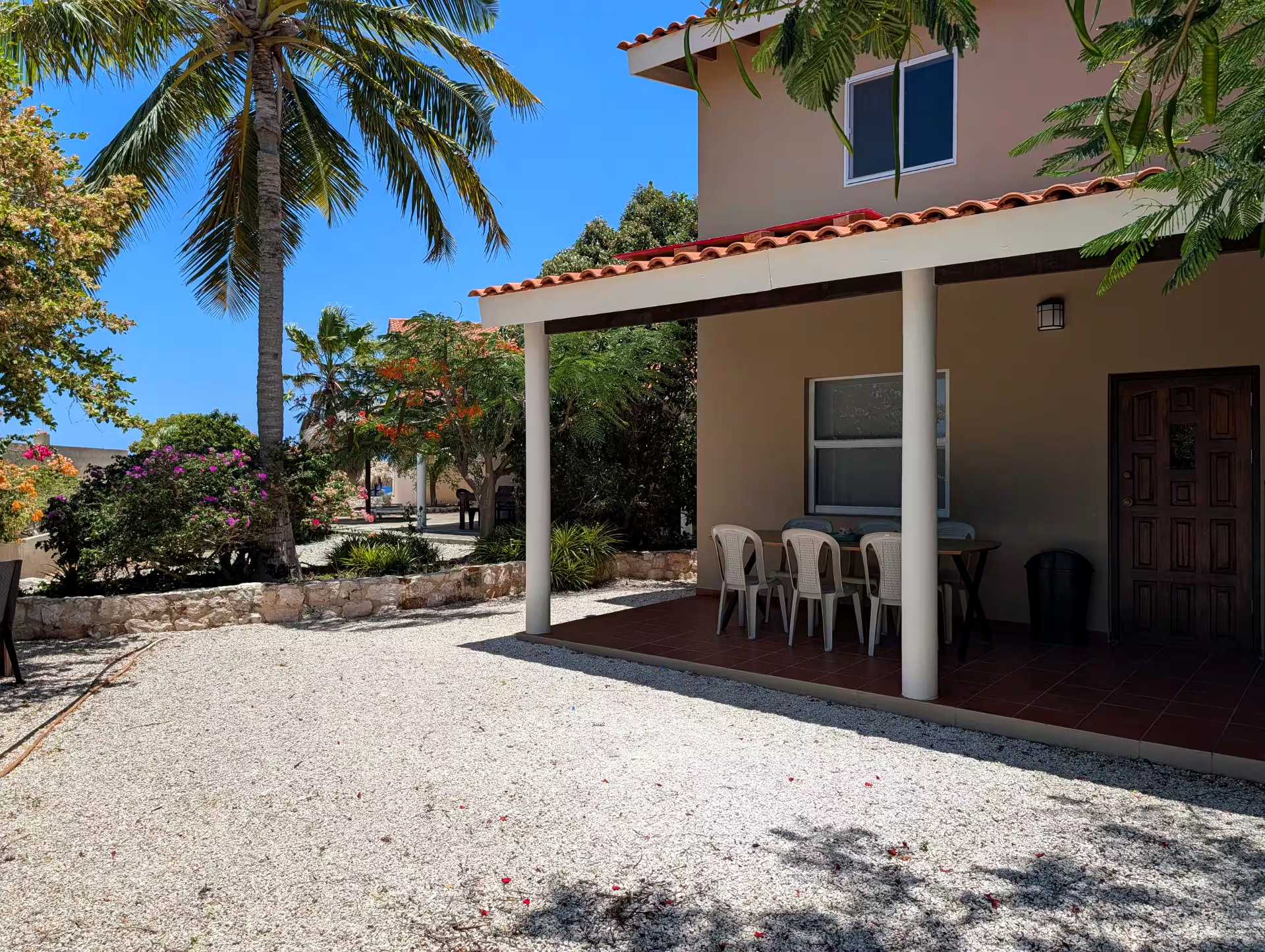 Huisje 21 seen from the garden, with the covered veranda, outdoor dining table and palm trees